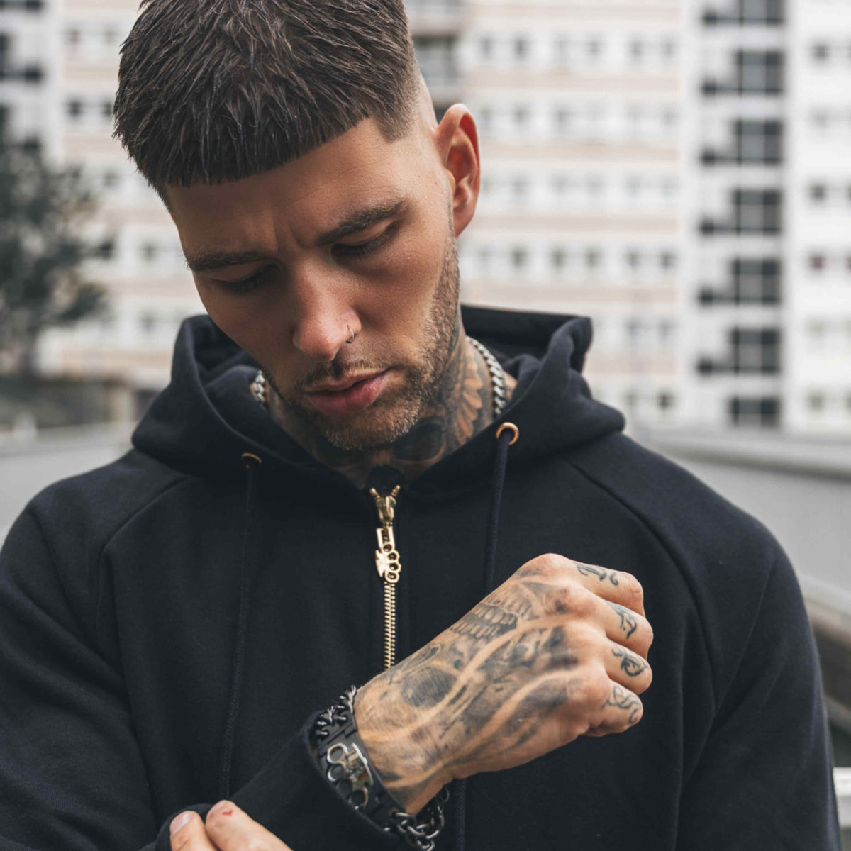 Primer plano de la sudadera Cupid with gun negra con cremallera dorada, llevada por modelo tatuado