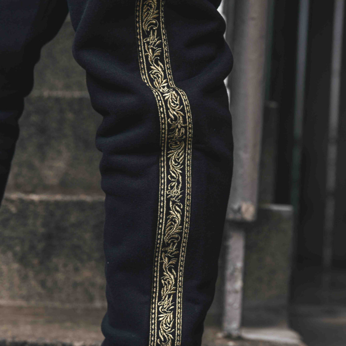 Nahaufnahme des goldenen Meander Stickbands entlang des Beins der schwarzen MVL Jogginghose