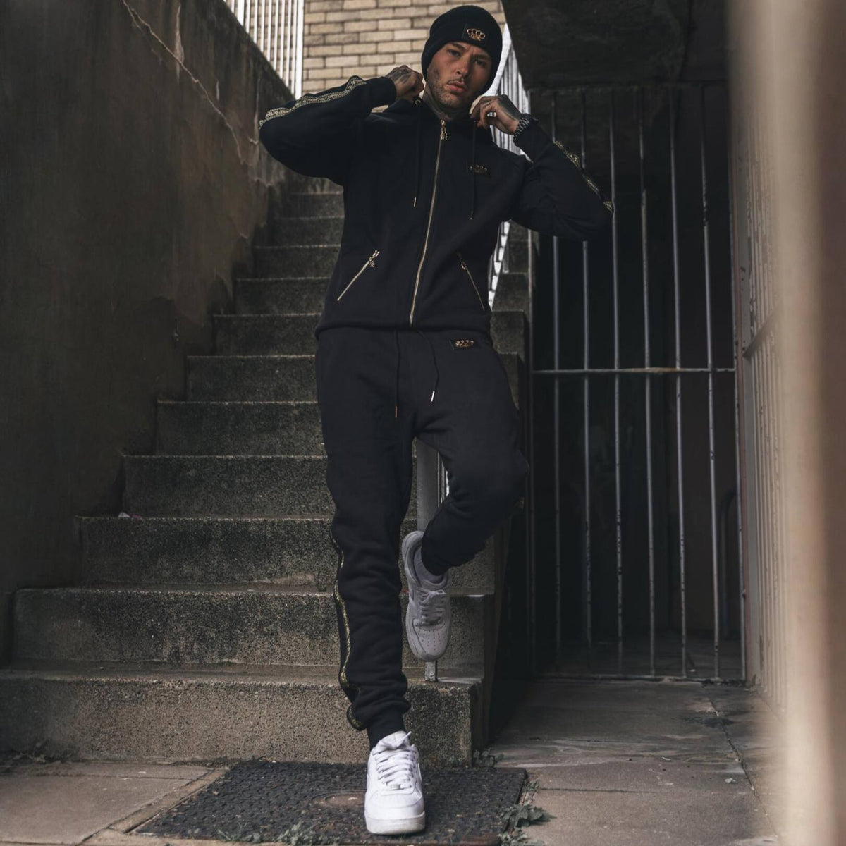 Model im MVL Meander Hoodie und Jogginghose auf einer Außentreppe, mit weißen Sneakers