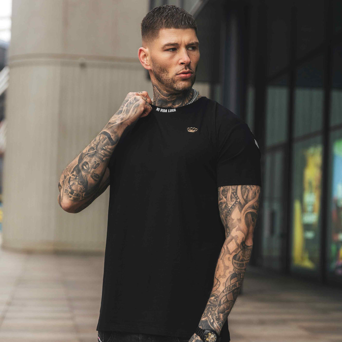 Model wearing the black MVL FTS T-shirt, front with small logo, in a city street