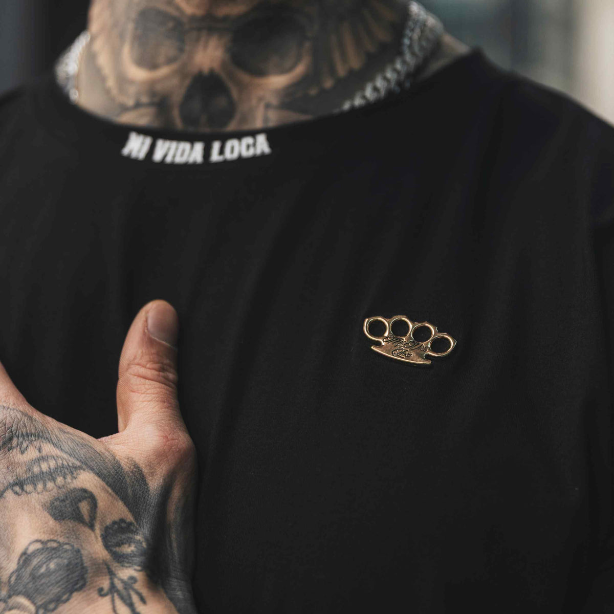 Close-up of the gold MVL logo and white Mi Vida Loca lettering in the collar of the black FTS T-shirt