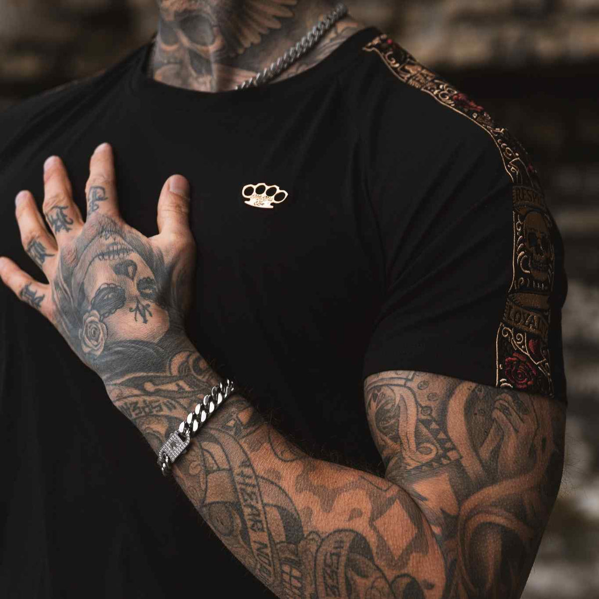 Gros plan du logo MVL doré sur la poitrine et de la bande de manche LFR du T-shirt noir, porté