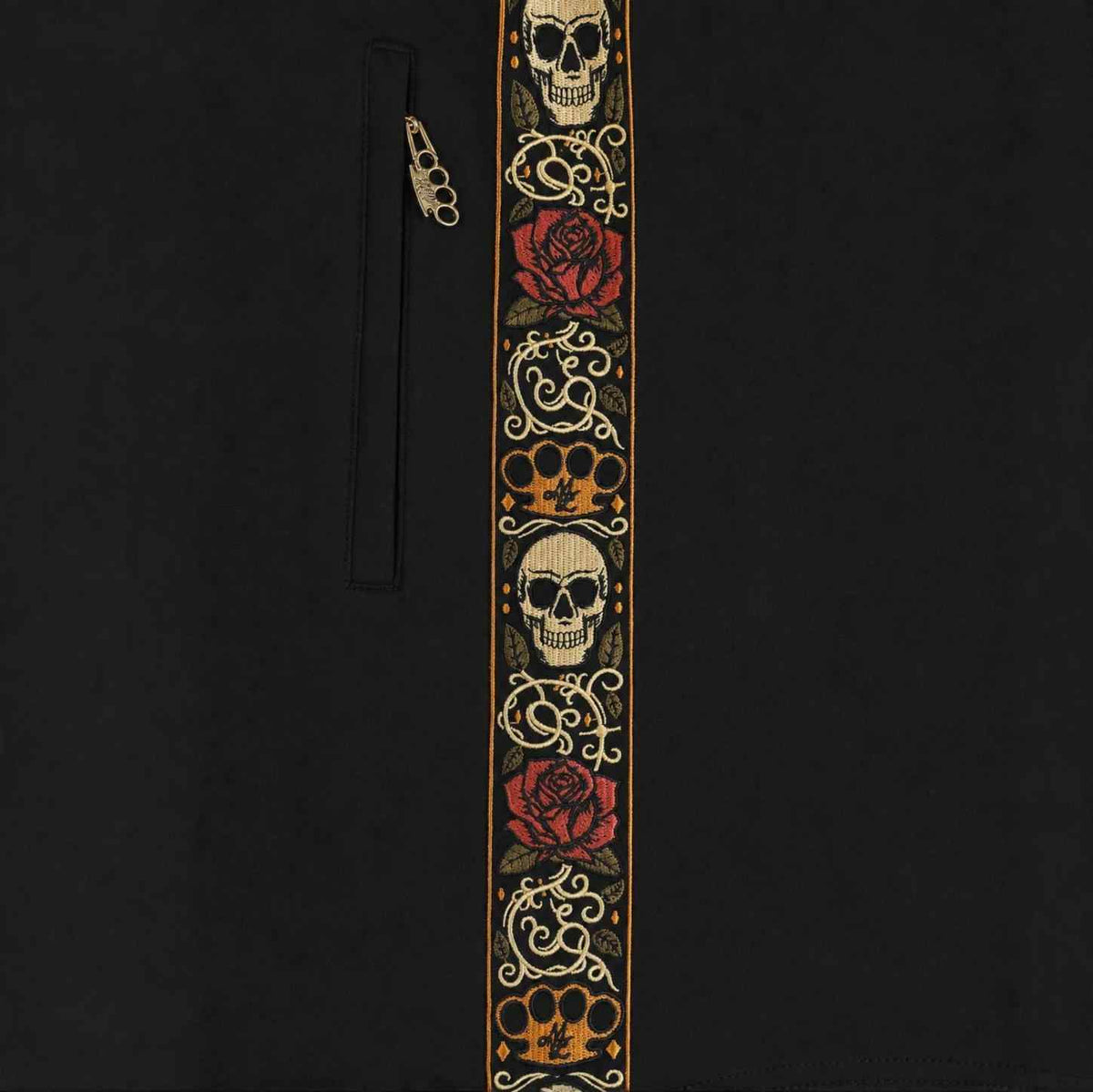 Primo piano della banda ricamata Calavera con teschi, rose e logo MVL accanto alla zip della tasca