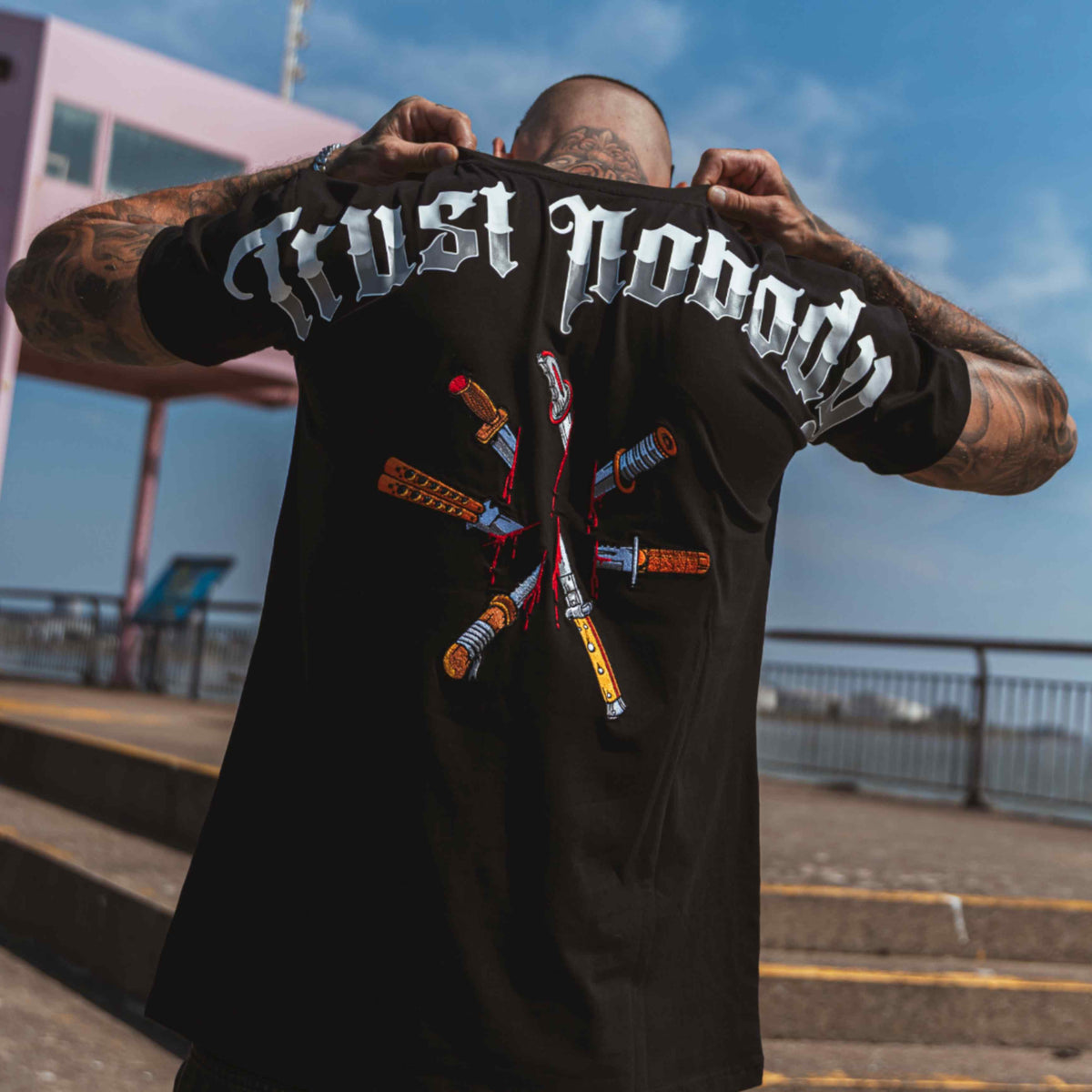 Model toont de Trust nobody backprint met messen op de rug van het zwarte T-shirt