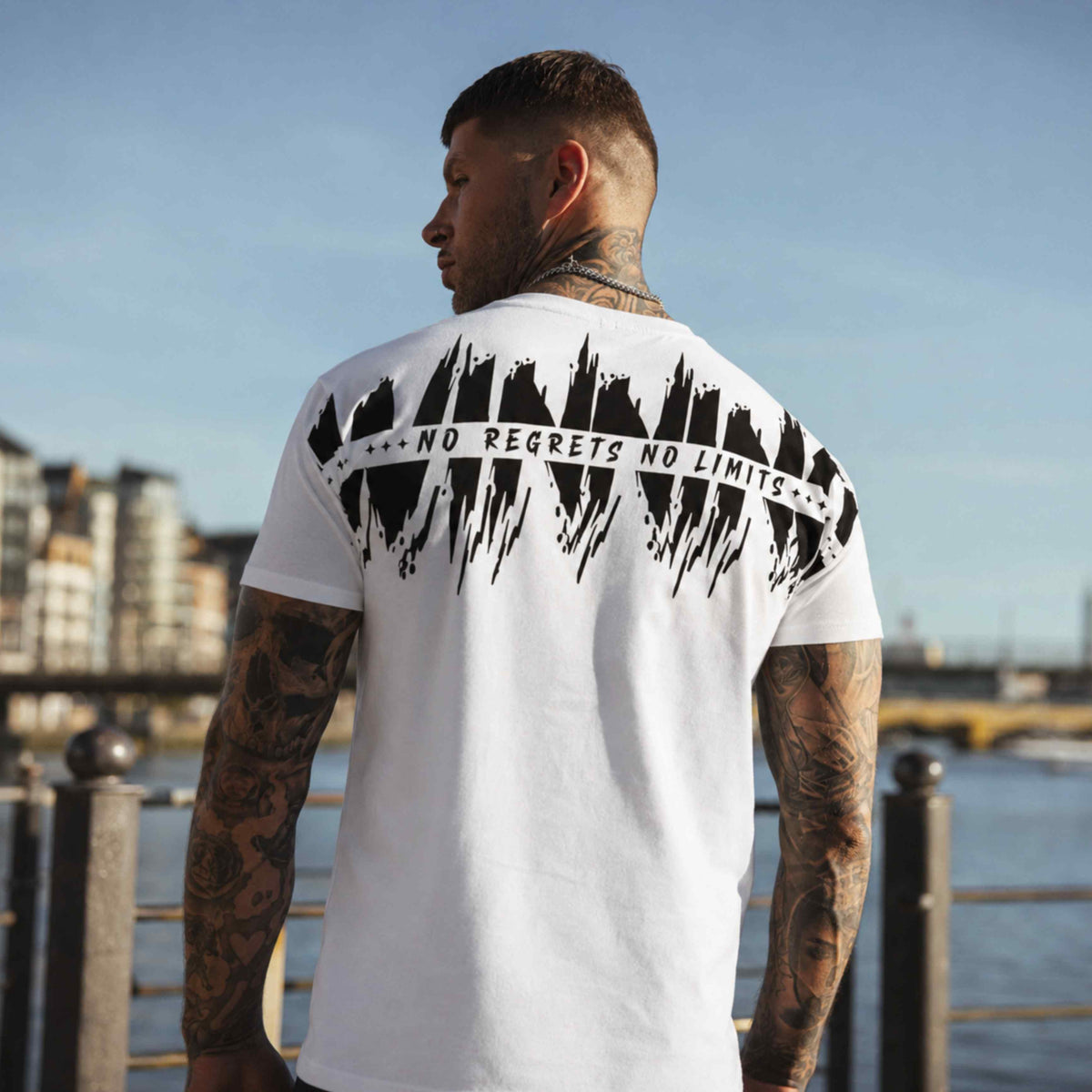 Modello di spalle nella T-shirt MVL Winning bianca con stampa sul retro in riva all'acqua