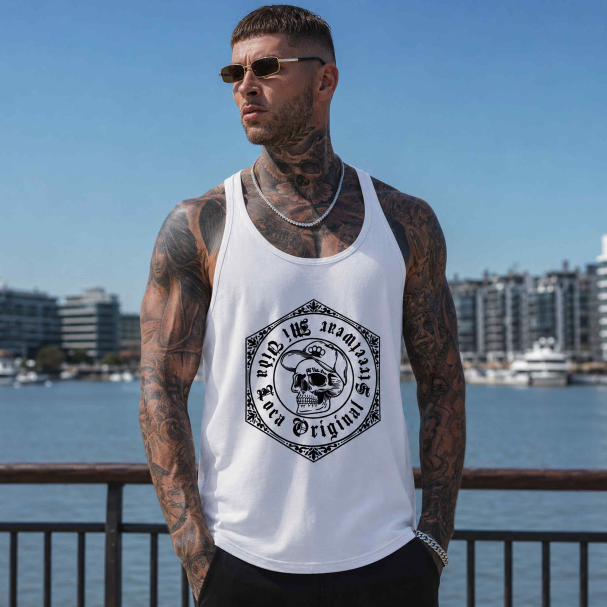 Modelo con camiseta de tirantes MVL Original streetwear blanca con estampado de calavera junto a una barandilla, puerto al fondo