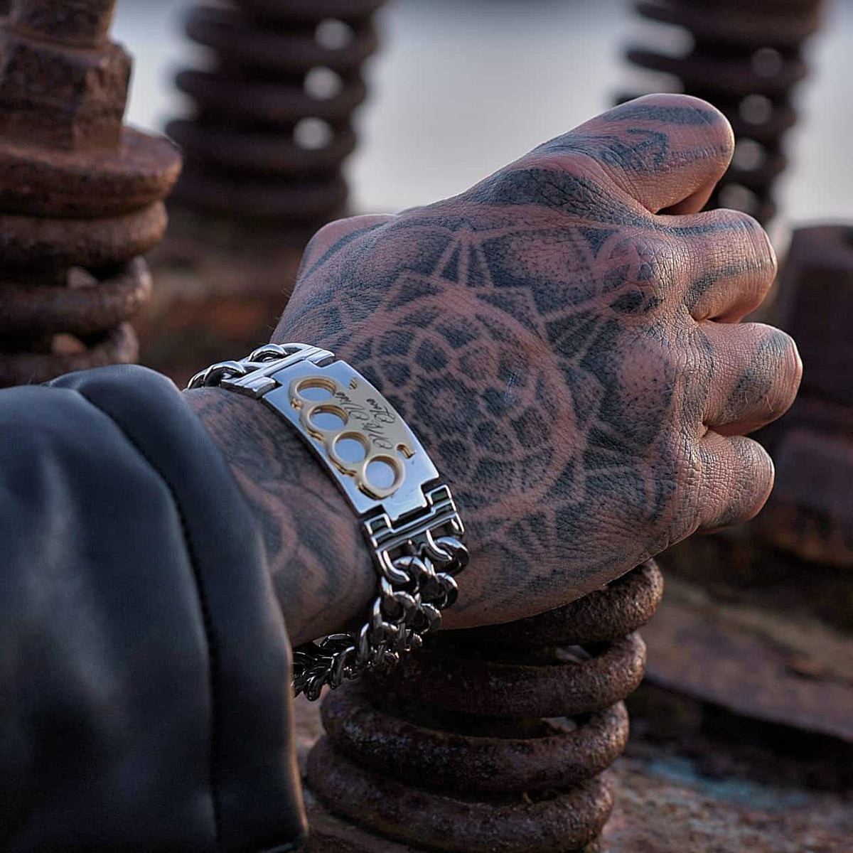 Bracelet MVL argent/or sur une main tatouée posée sur des spirales de métal rouillé