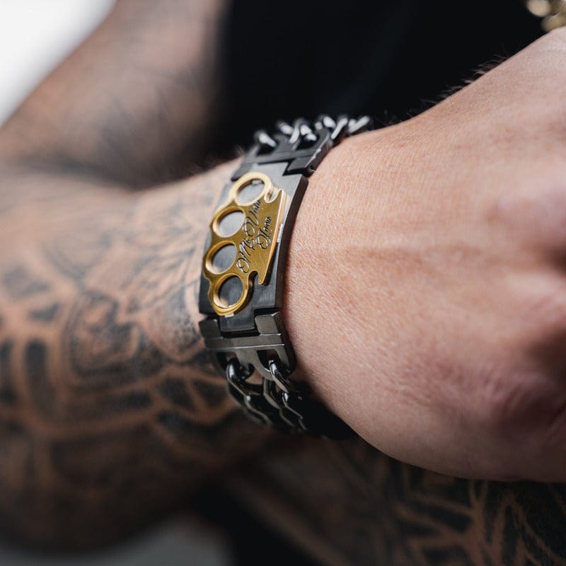 MVL bracelet in black/gold on the wrist of a tattooed arm, gold MVL logo in view