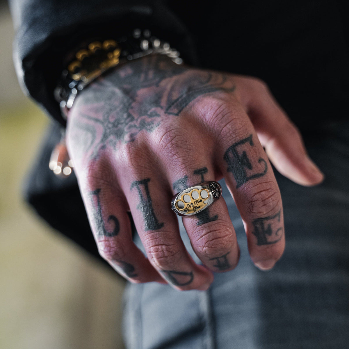 Anillo MVL Logo plateado en el dedo de una mano tatuada, primer plano